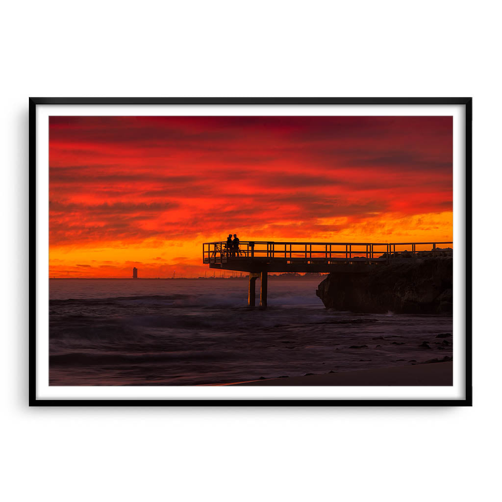 Couple watch sunset from the end of jetty in North Beach, Western Australia framed in black