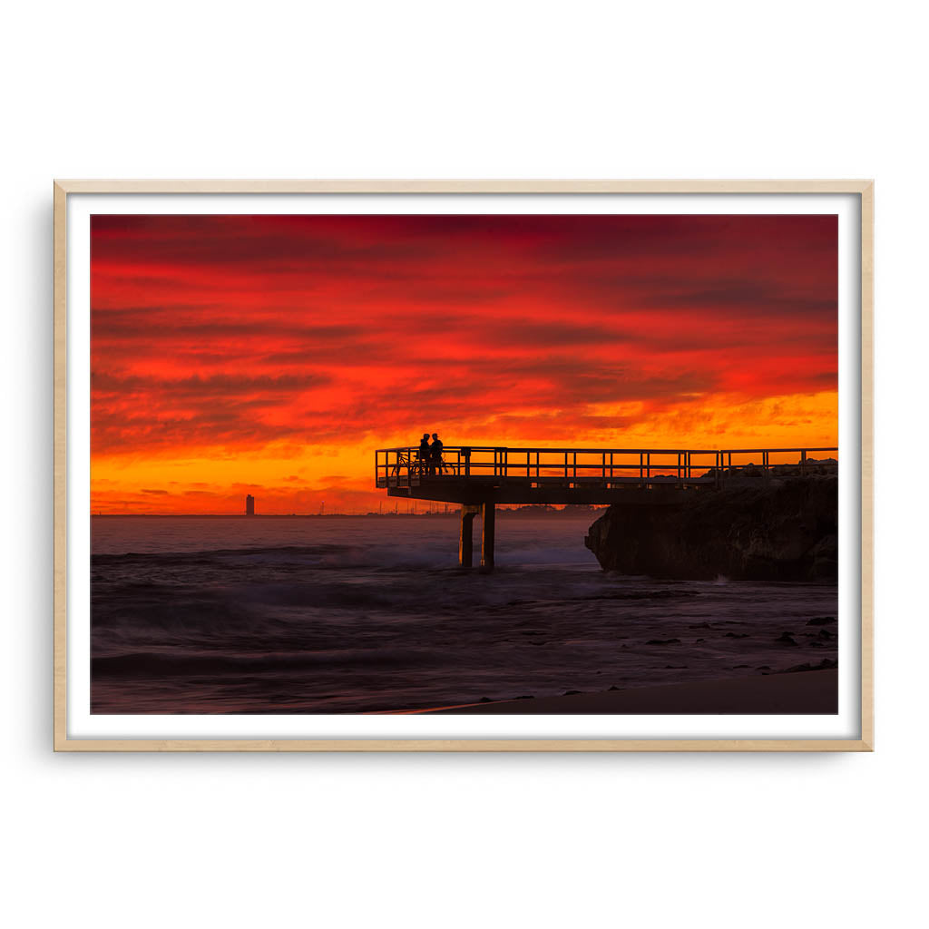 Couple watch sunset from the end of jetty in North Beach, Western Australia framed in raw oak